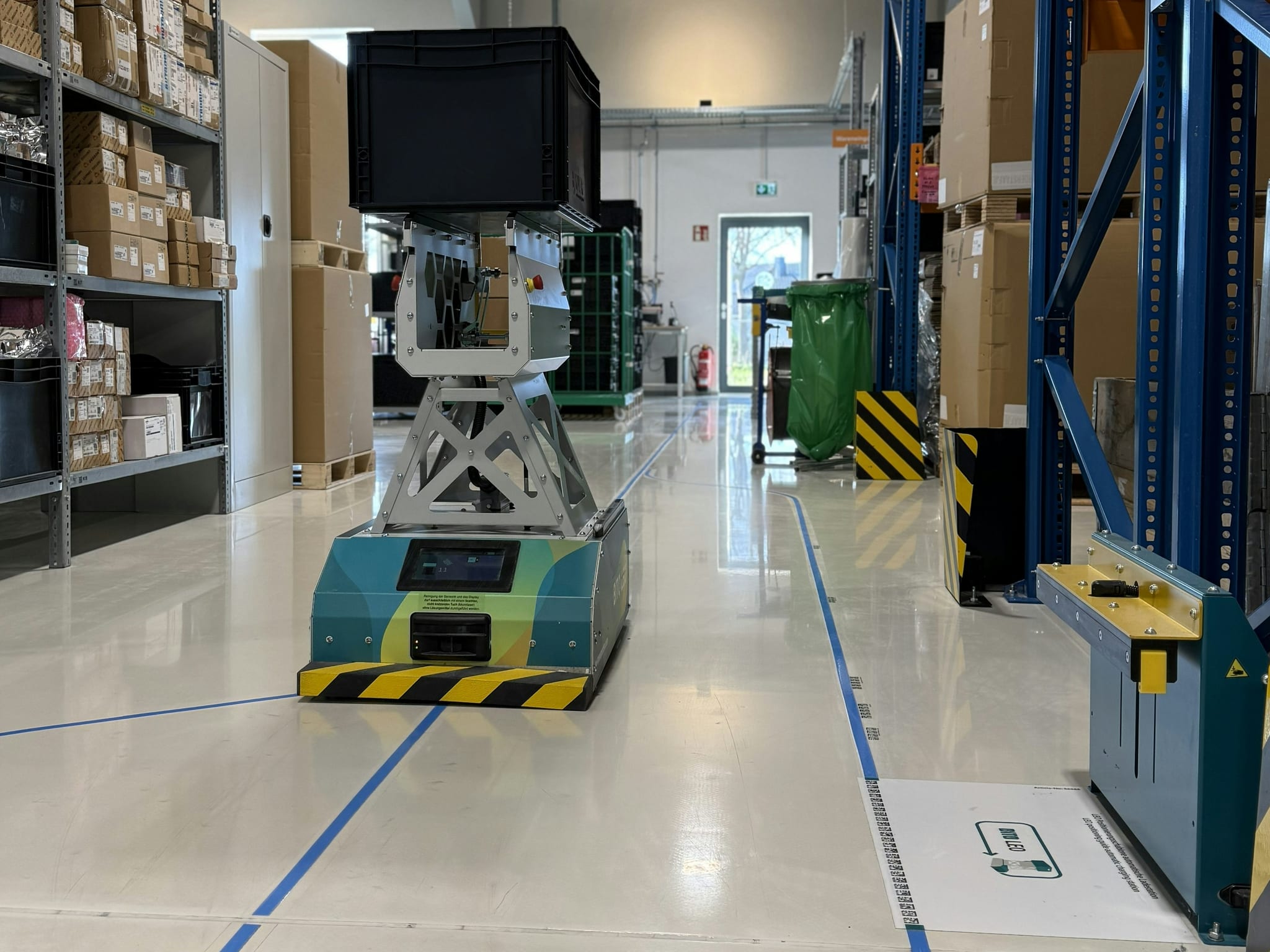 BITO LEO transportiert einen Behälter auf der Ringstrecke zwischen den Lagerregalen bei Newmatik